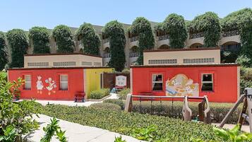 Un patio con dos edificios coloridos, uno rojo y otro amarillo, rodeado de follaje y un cielo despejado.