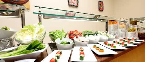 Un bufé con ensaladas y aperitivos variados, incluyendo sushi y bandejas de verduras.