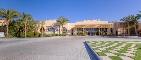 A hotel entrance with palm trees, a checkered lawn, and a clear blue sky.