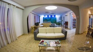 Un vestíbulo de hotel con un sofá, una mesa de centro con revistas, un televisor y una estantería.