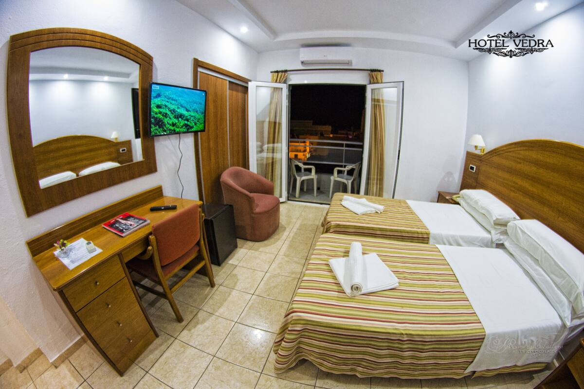 A hotel room with a bed, a desk, a chair, a television, and a balcony.