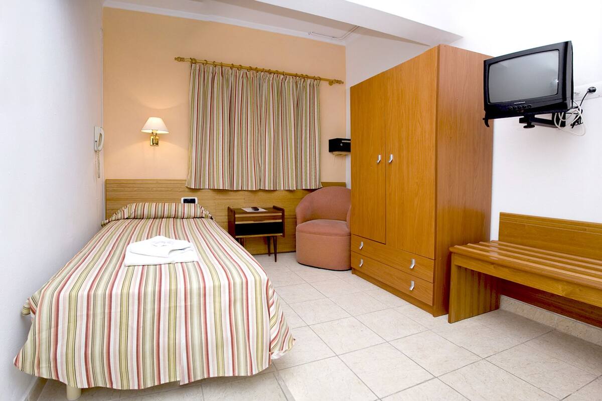 A hotel room with a bed, a desk, a chair, a wardrobe, and a television.