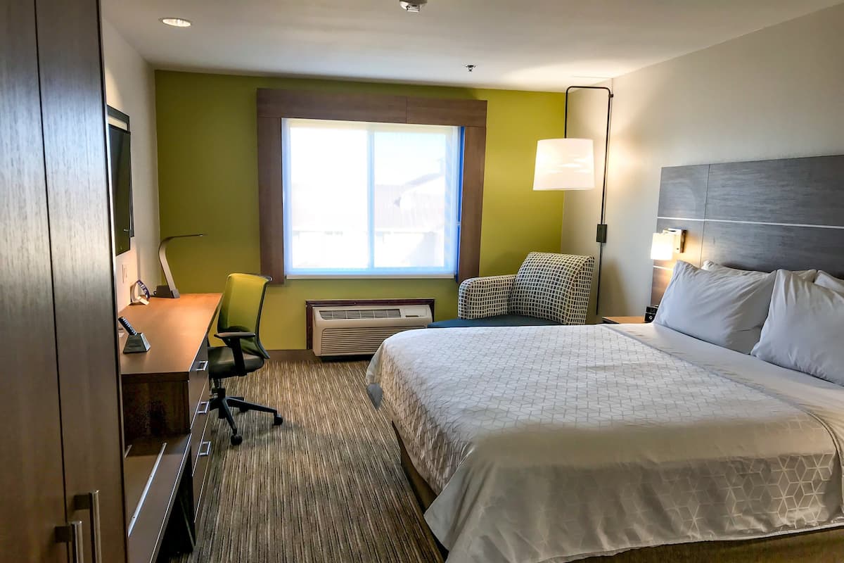 A hotel room with a bed, a desk with a chair, a window, and a lamp.