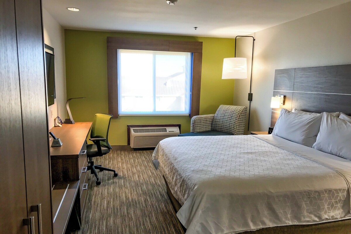 A hotel room with a bed, desk, chair, lamp, and a window.