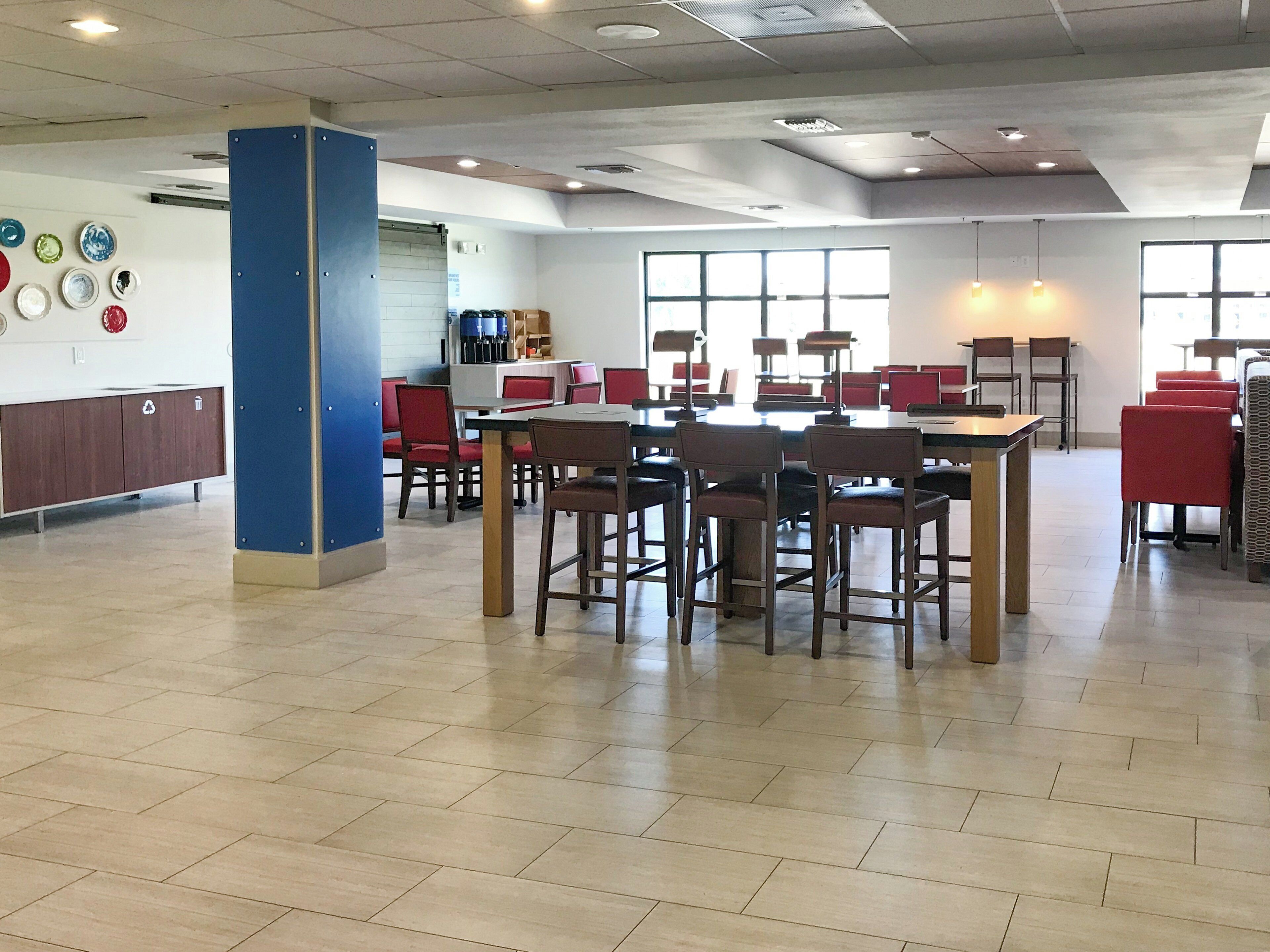 A spacious indoor area with multiple tables and chairs, a blue pillar, and a wall with various items.