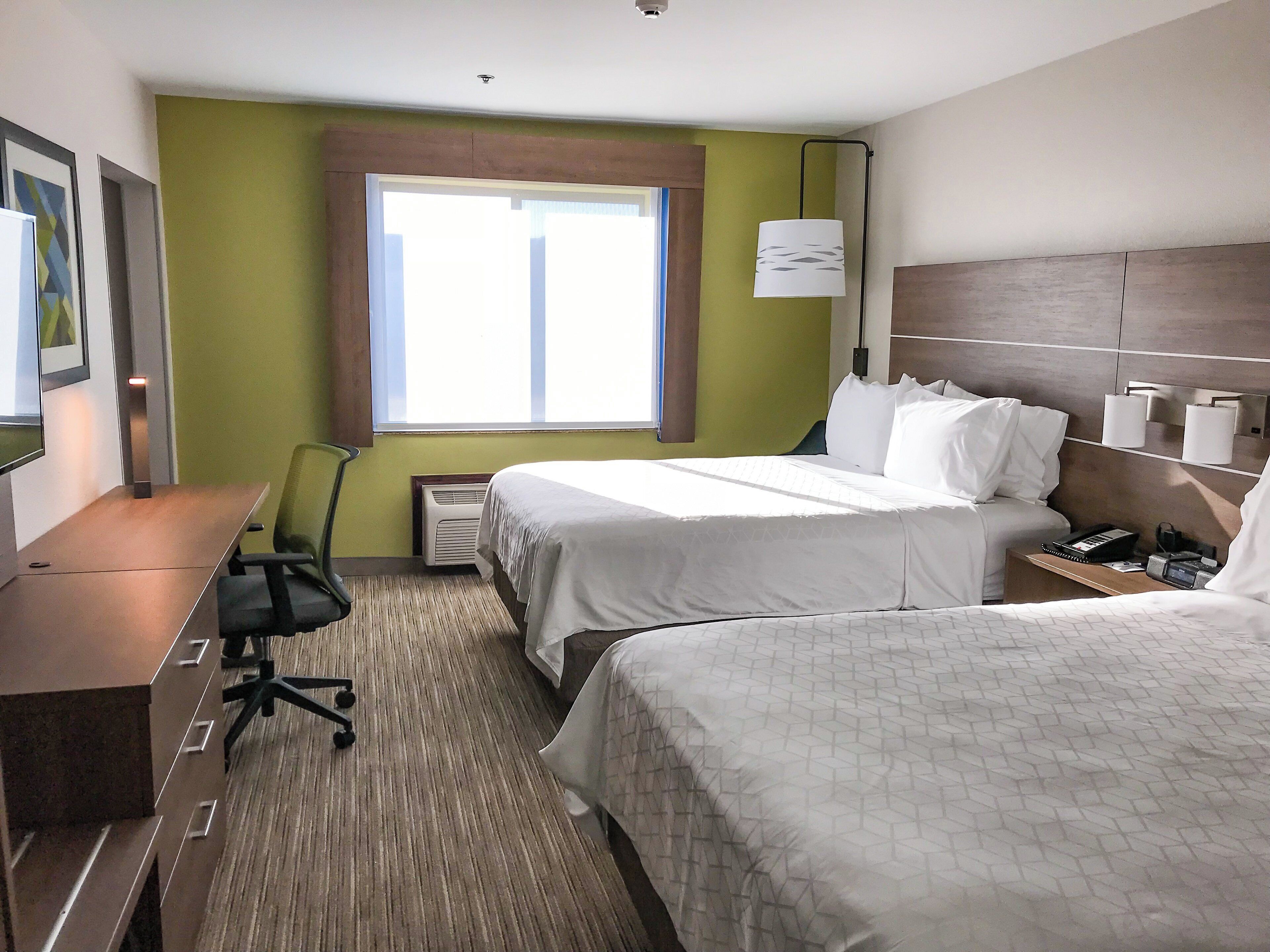 A hotel room with a bed, a desk, a chair, a window, and a lamp.
