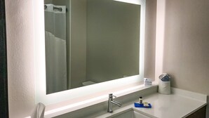 Une salle de bain avec un grand miroir, un lavabo, un distributeur de serviettes et un distributeur de savon.