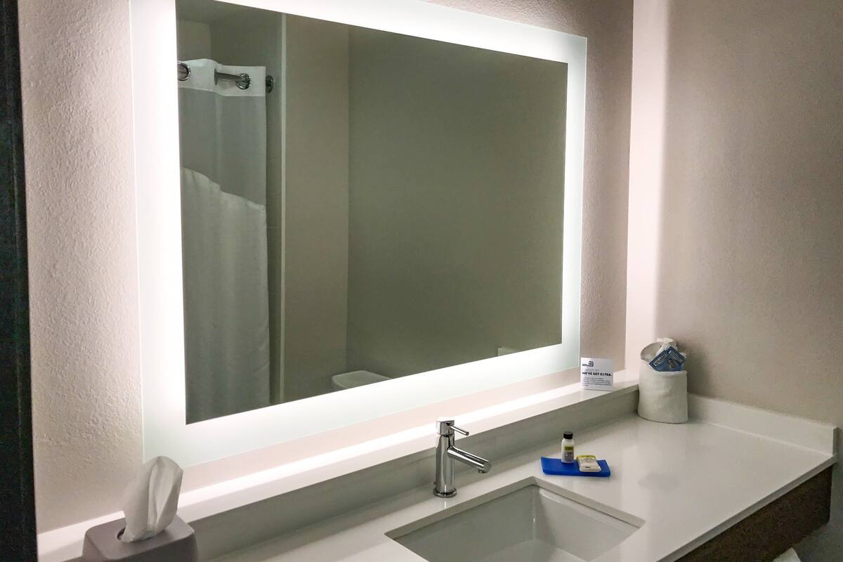 A bathroom with a large mirror, a sink, a towel dispenser, and a soap dispenser.