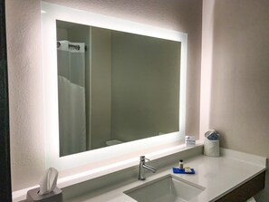 A bathroom with a large mirror, a sink, a towel dispenser, and a soap dispenser.