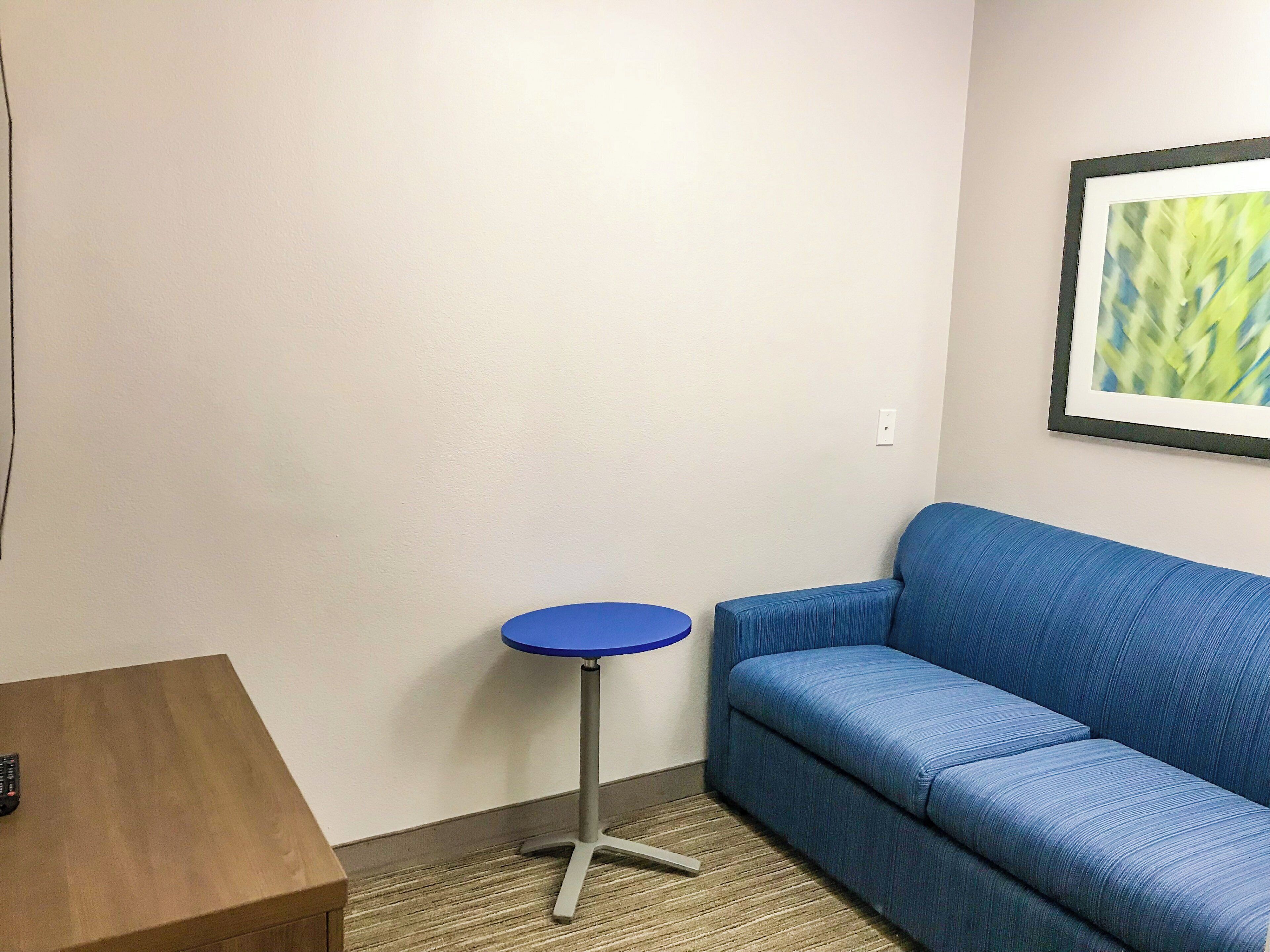 A room with a blue sofa, a small round table, and a framed picture on the wall.