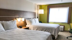 Une chambre d’hôtel avec deux lits, une table de chevet, une lampe et une fenêtre avec des stores.