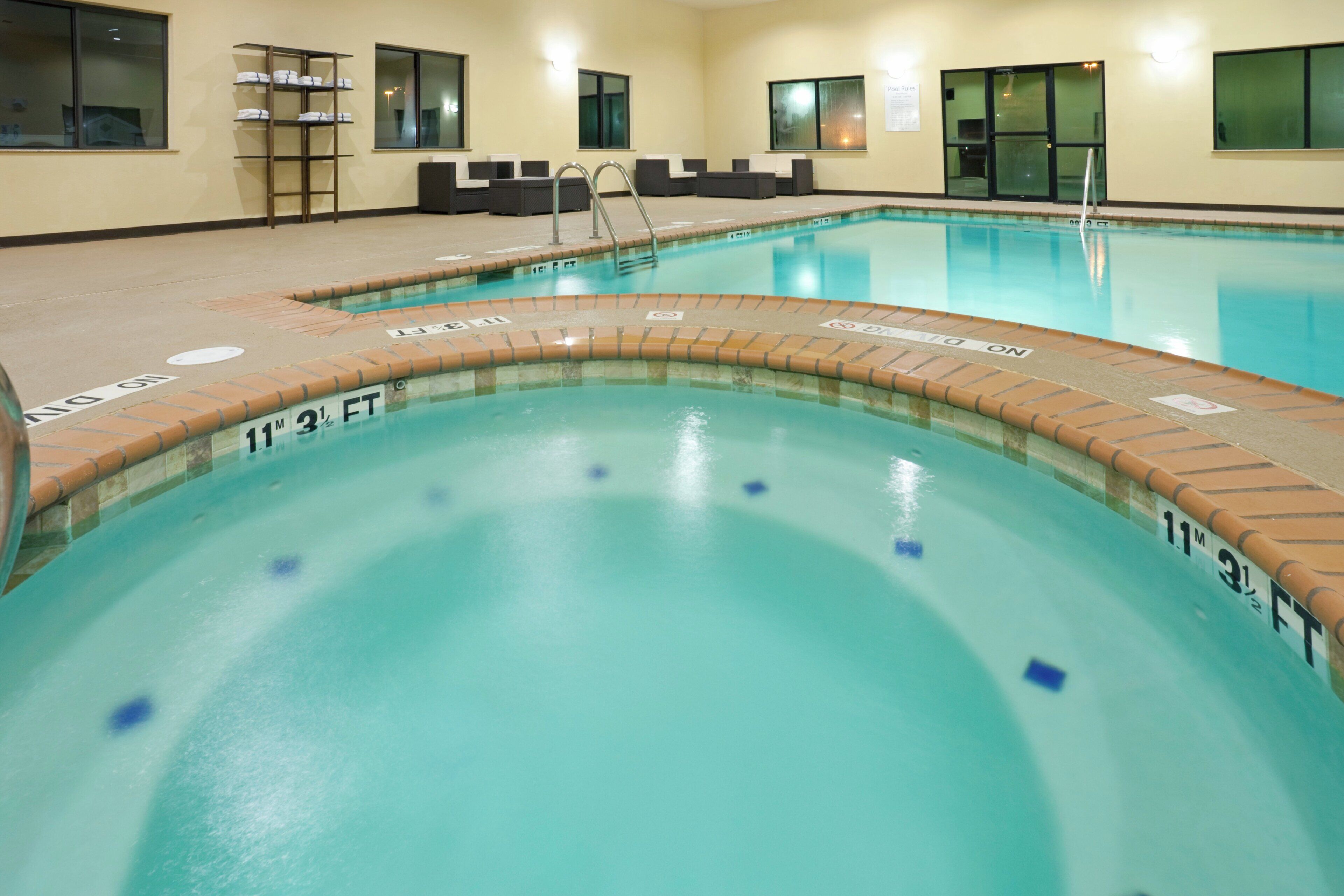 A swimming pool with clear water, marked depth lines, and a lounge area with seating.