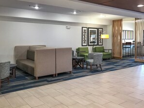 A hotel lobby with a patterned sofa, a green armchair, a small table, and a lamp. - Holiday Inn Express & Suites Lubbock West by IHG (Lubbock)