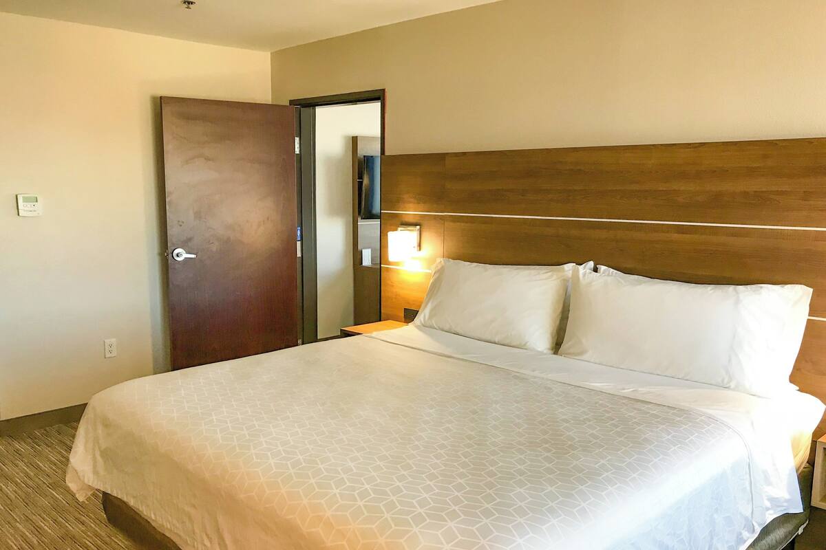 A hotel room with a large bed, wooden headboard, and a nightstand with a lamp.