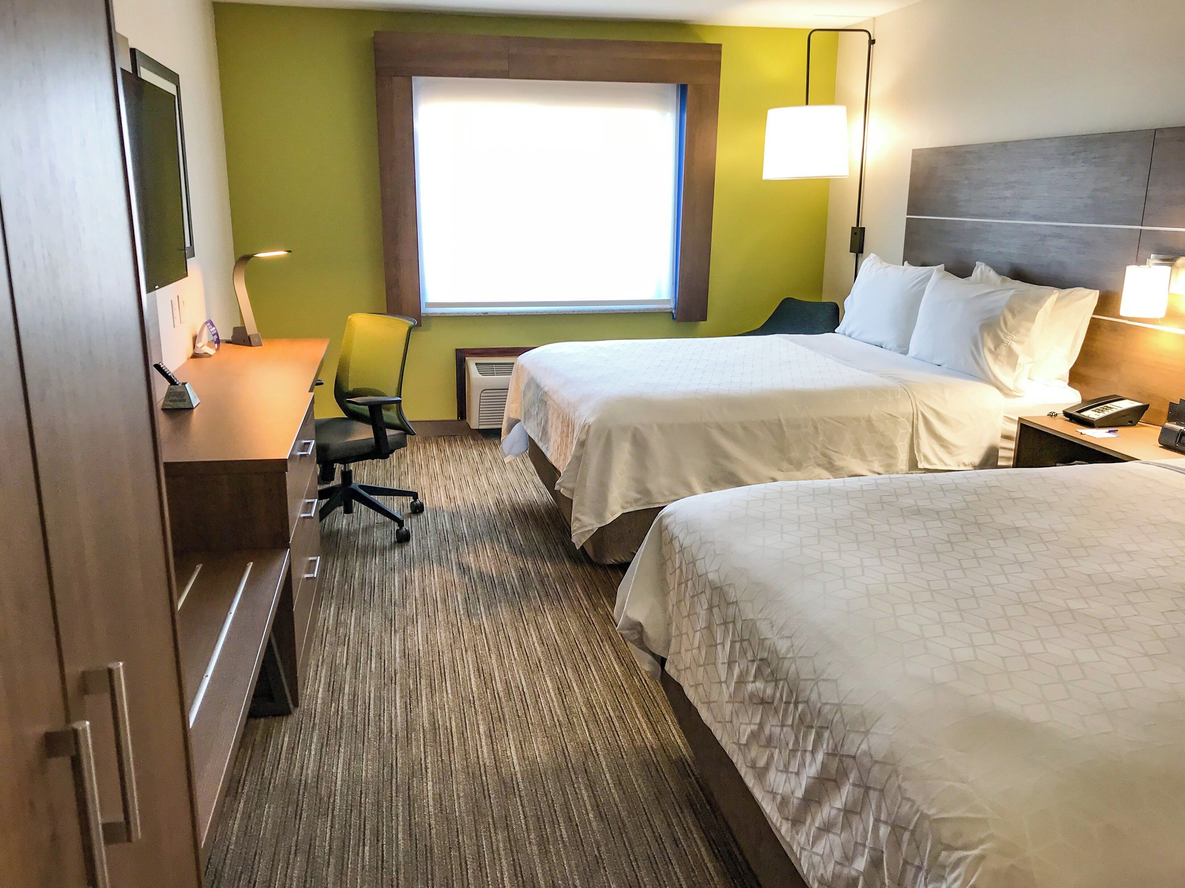 Habitación de hotel con dos camas, un escritorio, una silla, un ventanal y una lámpara.