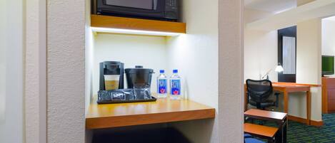 Habitación de hotel compacta con microondas, cafetera y agua embotellada en un estante.