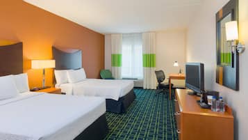 Una habitación de hotel con dos camas, un escritorio con computadora, un televisor y un espejo.