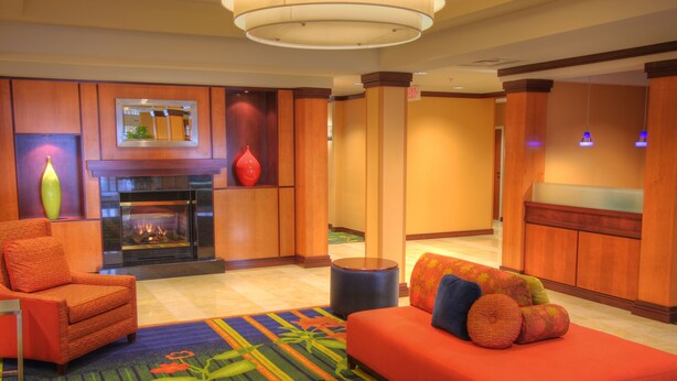 A modern hotel lobby with a fireplace, a sofa with colorful cushions, and a patterned carpet.