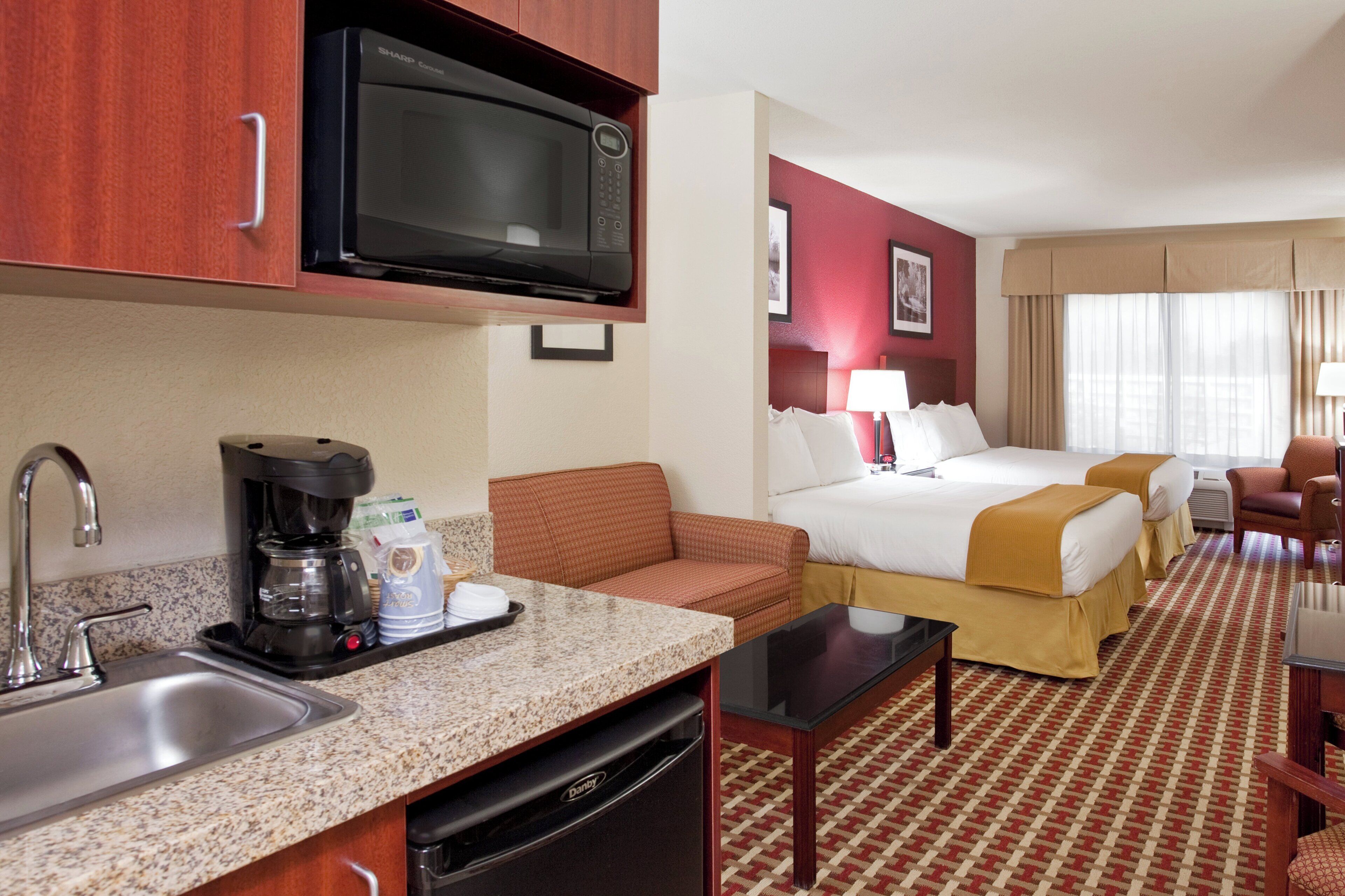 Una habitación de hotel con kitchenette, dos camas, un sofá y una mesa de comedor.