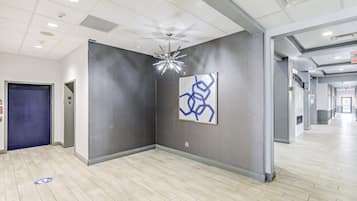 Un moderno vestíbulo de hotel con una puerta azul, una obra de arte abstracta en la pared y una lámpara de techo original.