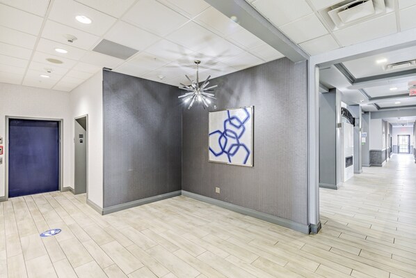 Un moderno vestíbulo de hotel con una puerta azul, una obra de arte abstracta en la pared y una lámpara de techo original.