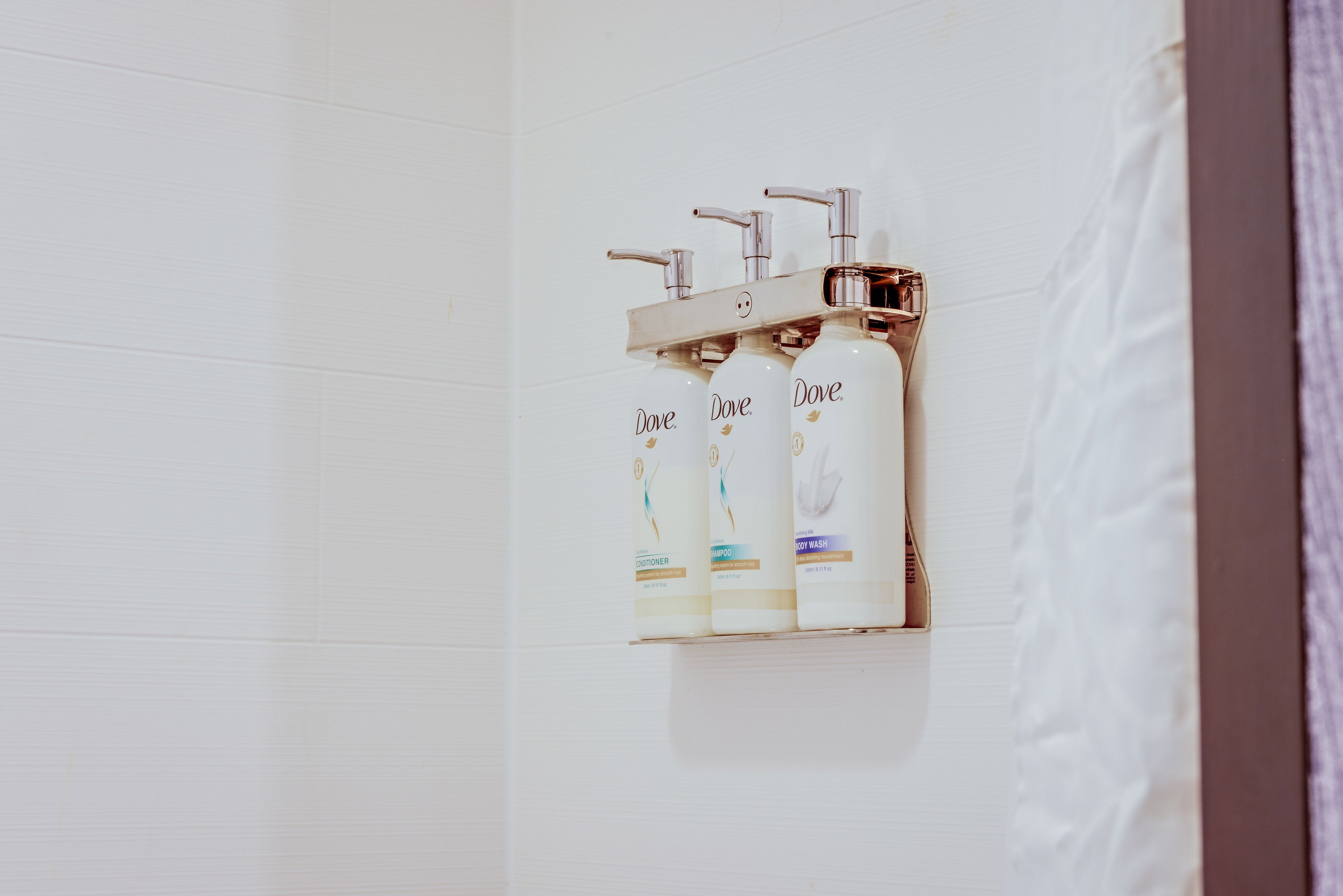A bathroom with three Dove shampoo bottles on a wall-mounted shelf.