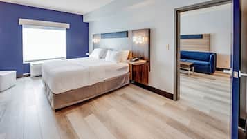 Quarto de hotel moderno com cama grande, mesas de cabeceira, um banco embutido e vista para o quarto vizinho.