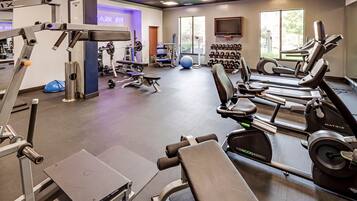Un gimnasio con máquinas de cardio, equipo de levantamiento de pesas y un televisor montado en la pared.
