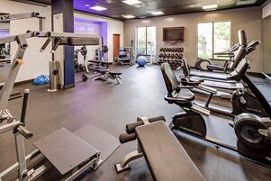 Een sportschool met cardioapparatuur, gewichthefmaterialen en een aan de muur bevestigde televisie.