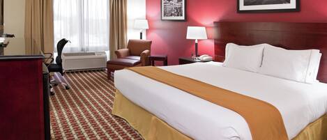 A hotel room with a large bed, a desk, a chair, a lamp, and two framed pictures on the wall.