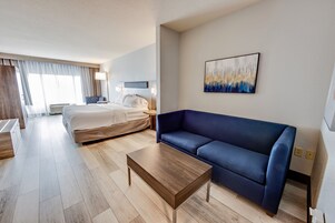 Een hotelkamer met een bed, een blauwe bank, een houten salontafel en een schilderij aan de muur.