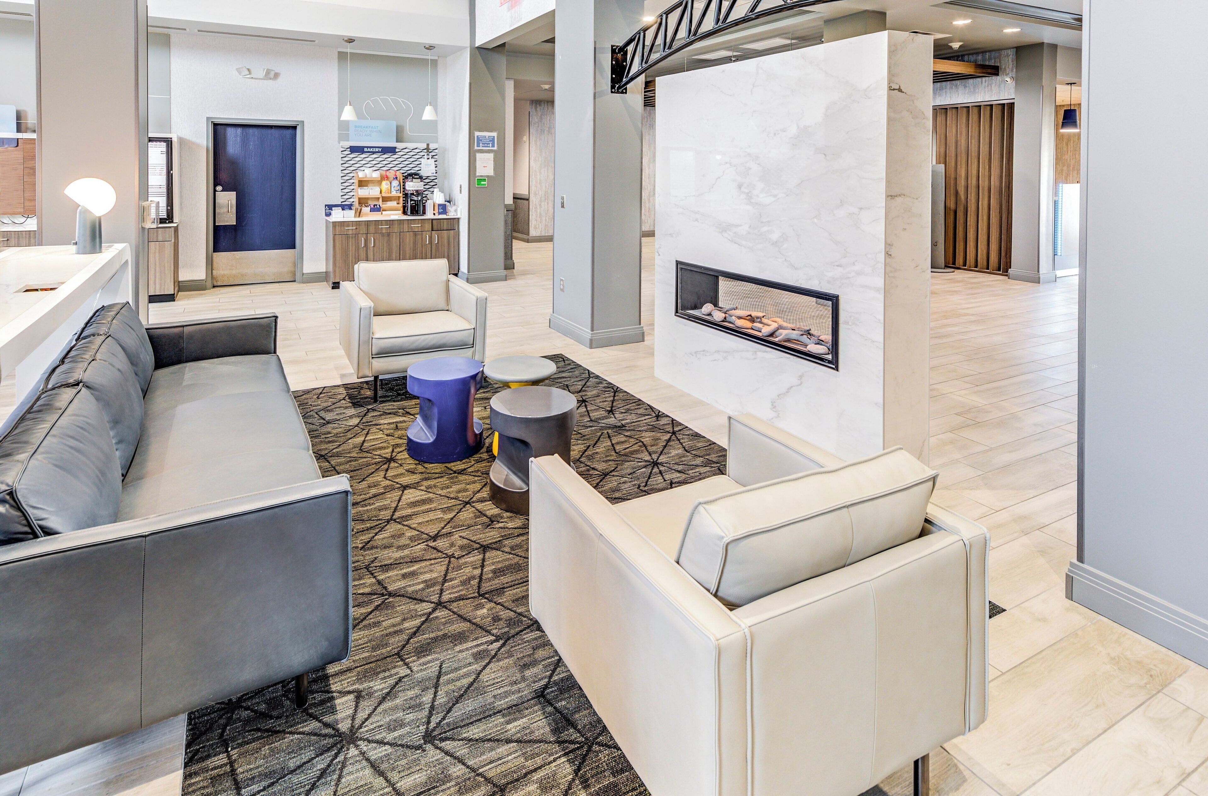 A modern hotel lobby with a seating area, a fireplace, and a bakery sign.