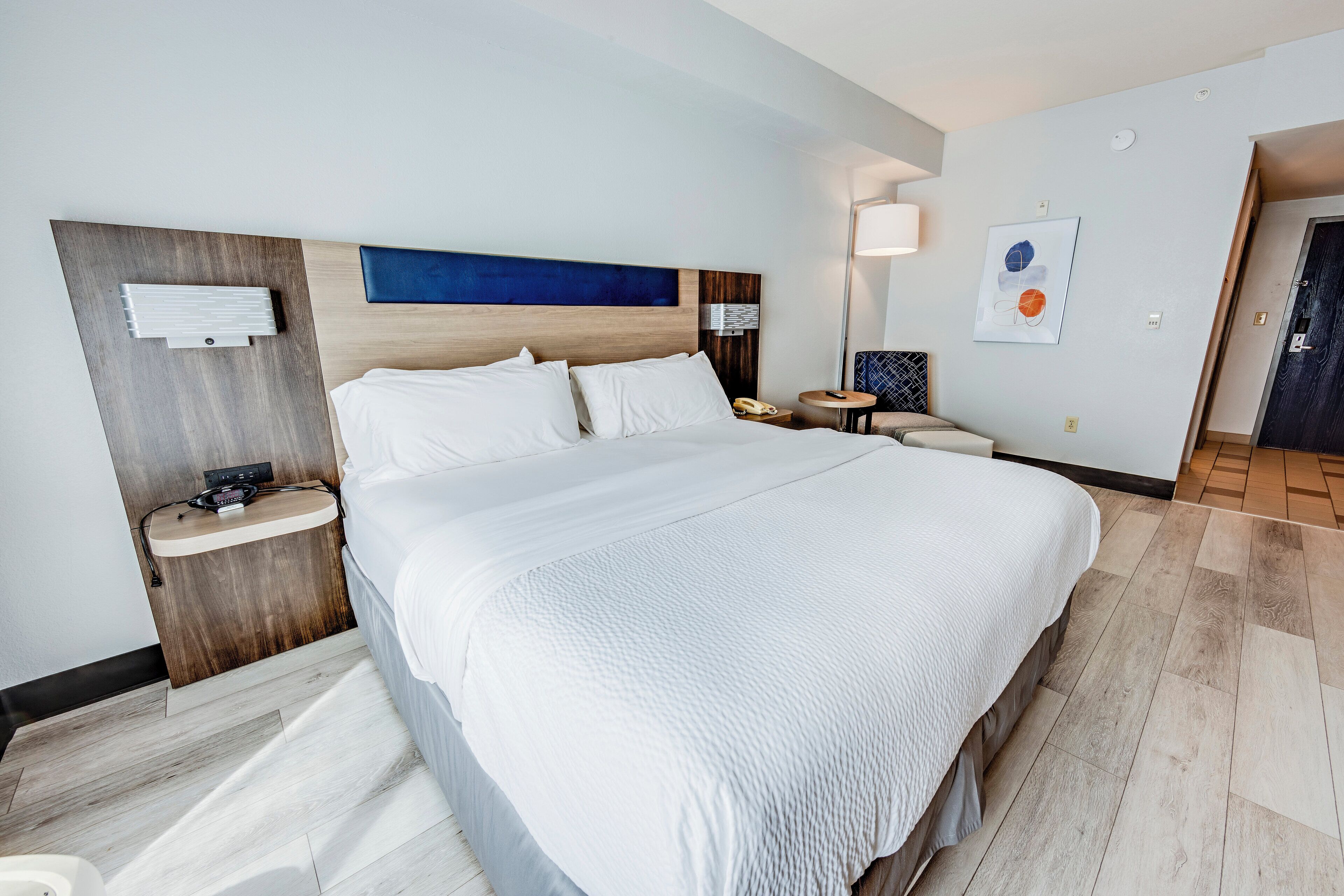 Ein Hotelzimmer mit einem großen Bett, Nachttischen, einer Wandleuchte und einem gerahmten Bild.