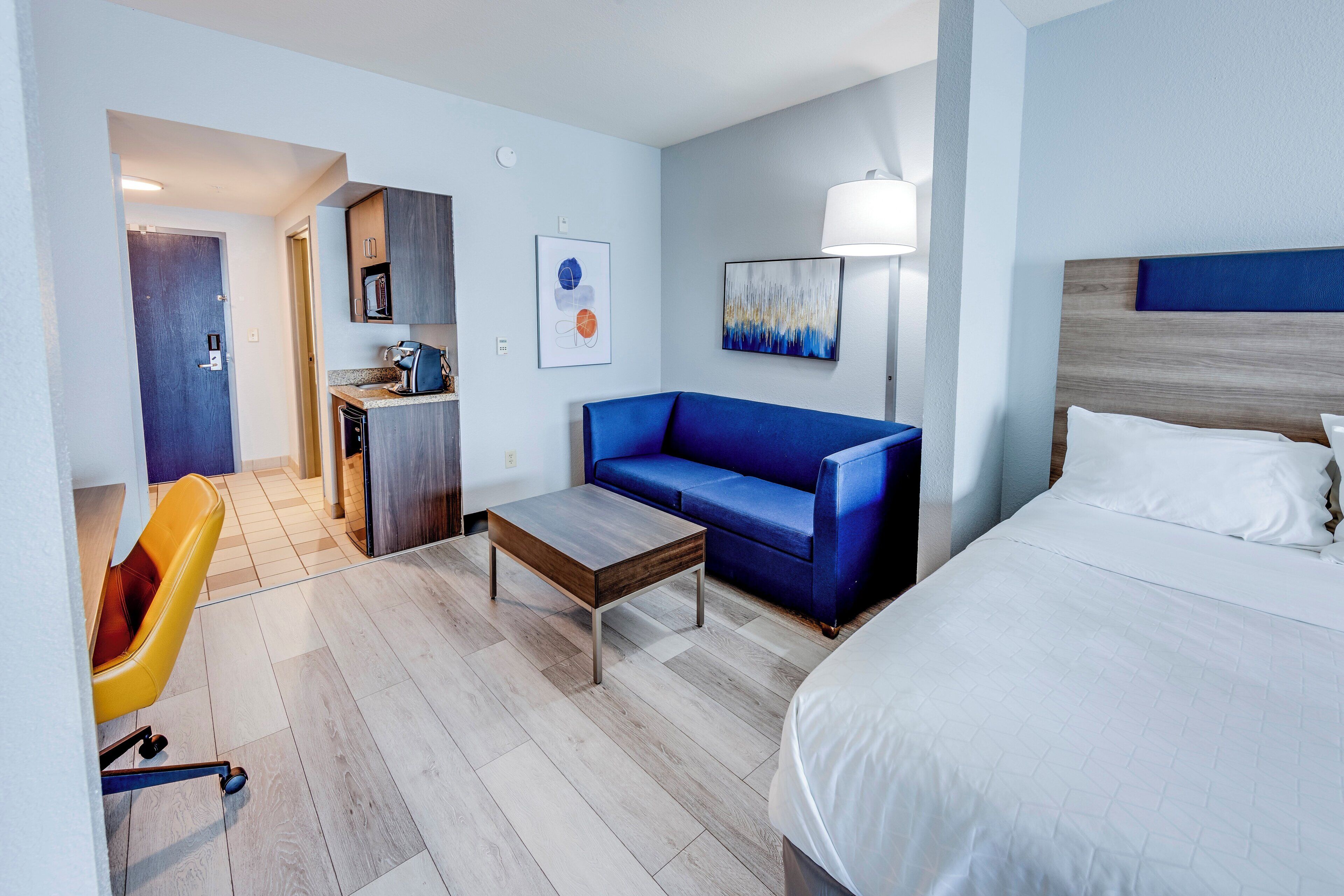 A hotel room with a bed, a sofa, a coffee table, a desk with a chair, a lamp, and artwork on the walls.