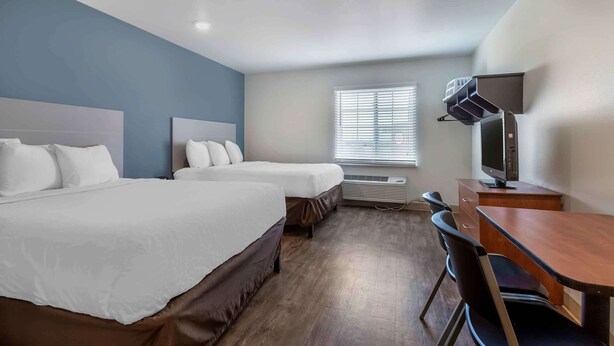 Habitación de hotel con dos camas, un escritorio, una silla, un televisor y una ventana con persianas.