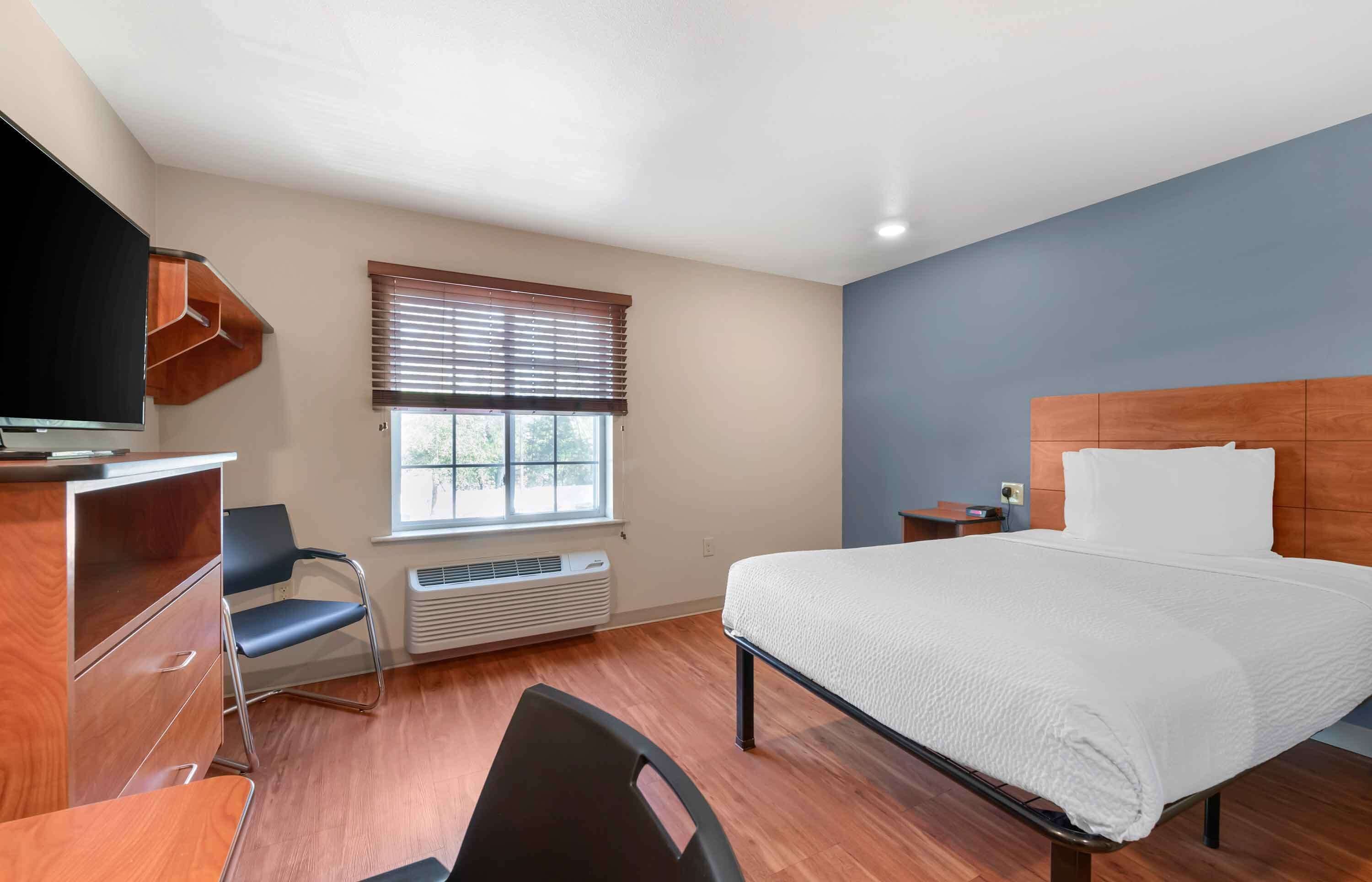 A hotel room with a bed, a desk, a chair, a television, and a window with blinds.