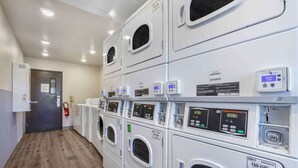 Un cuarto de lavado con varias lavadoras y secadoras, paneles de control y un extintor.