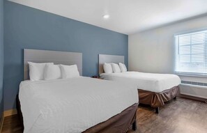 Une chambre d’hôtel avec deux lits, un mur d’accent bleu et une fenêtre avec des stores.