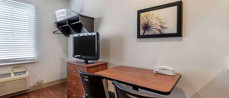 Una pequeña oficina con un escritorio, dos sillas, un monitor de computadora, un teléfono y un cuadro en la pared.