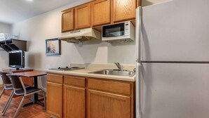 Cocina compacta con armarios de madera, microondas, refrigerador, lavamanos y un comedor con sillas.