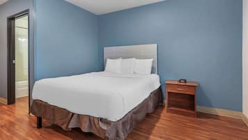 A bedroom with a large bed, a nightstand, and a door to a bathroom.