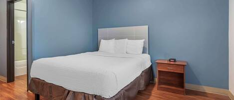 A bedroom with a large bed, a nightstand, and a door to a bathroom.