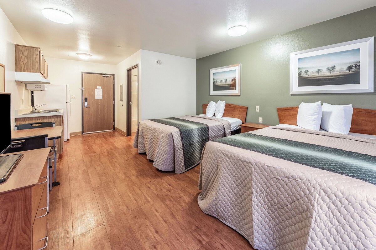 Une chambre d’hôtel avec deux lits, un bureau, une kitchenette et une porte donnant sur une autre pièce.