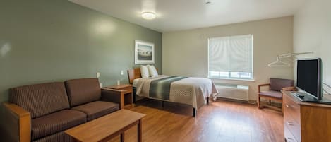 Habitación compacta con cama, sofá, televisor y ventana con persianas.