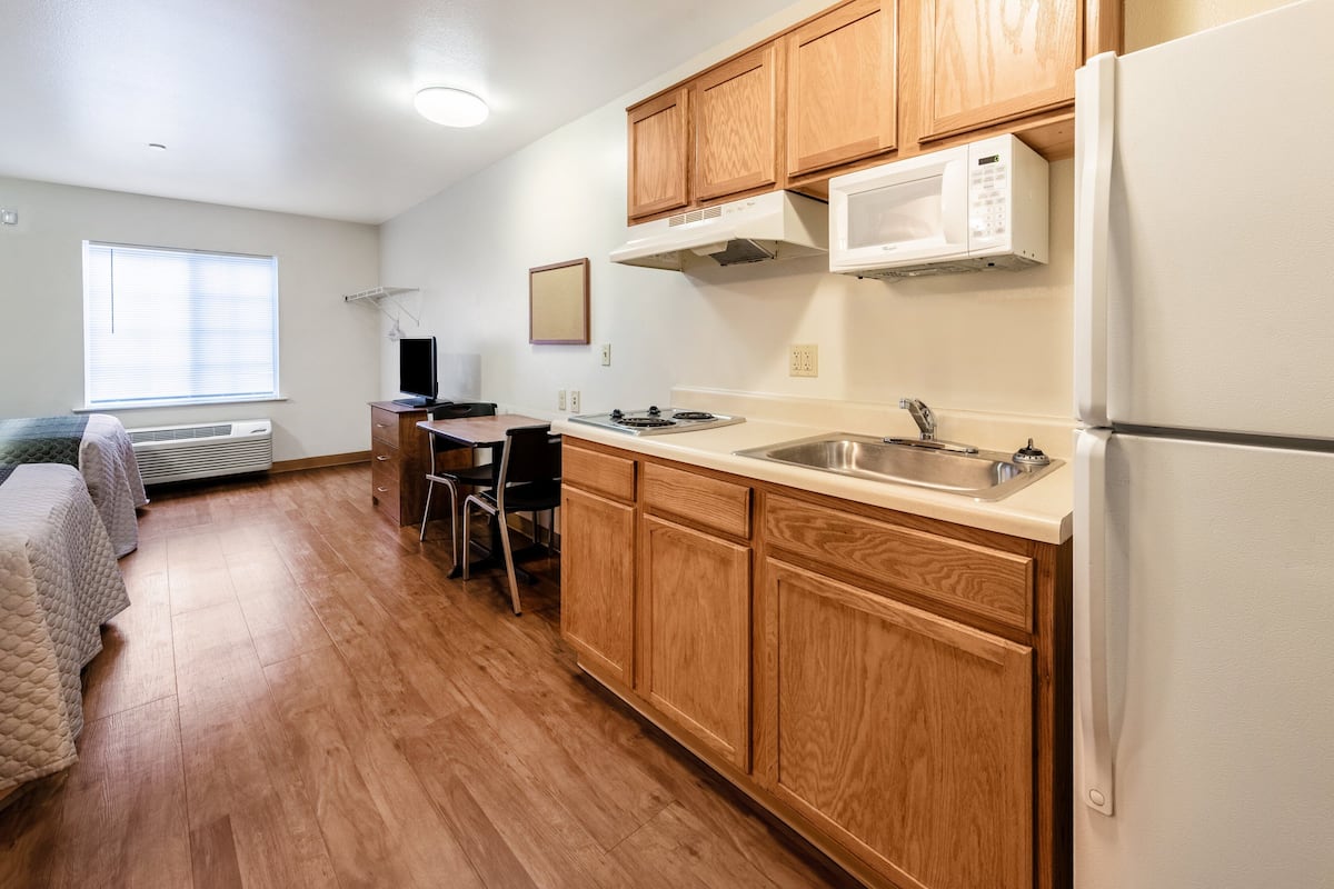 A compact kitchen with wooden cabinets, a microwave, a refrigerator, a sink, and a dining area with chairs.