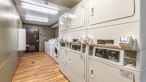 Een wasserette met meerdere wasmachines en drogers, een houten vloer en een deur aan het einde.