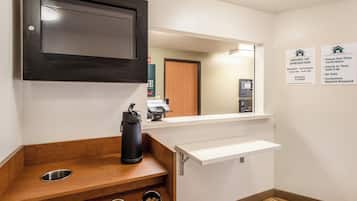 Ein Hotel-Empfangsbereich mit einer Rezeption, einem digitalen Bezahllterminal und einer an der Wand befestigten Infotafel mit Angaben zu Öffnungszeiten und Richtlinien.