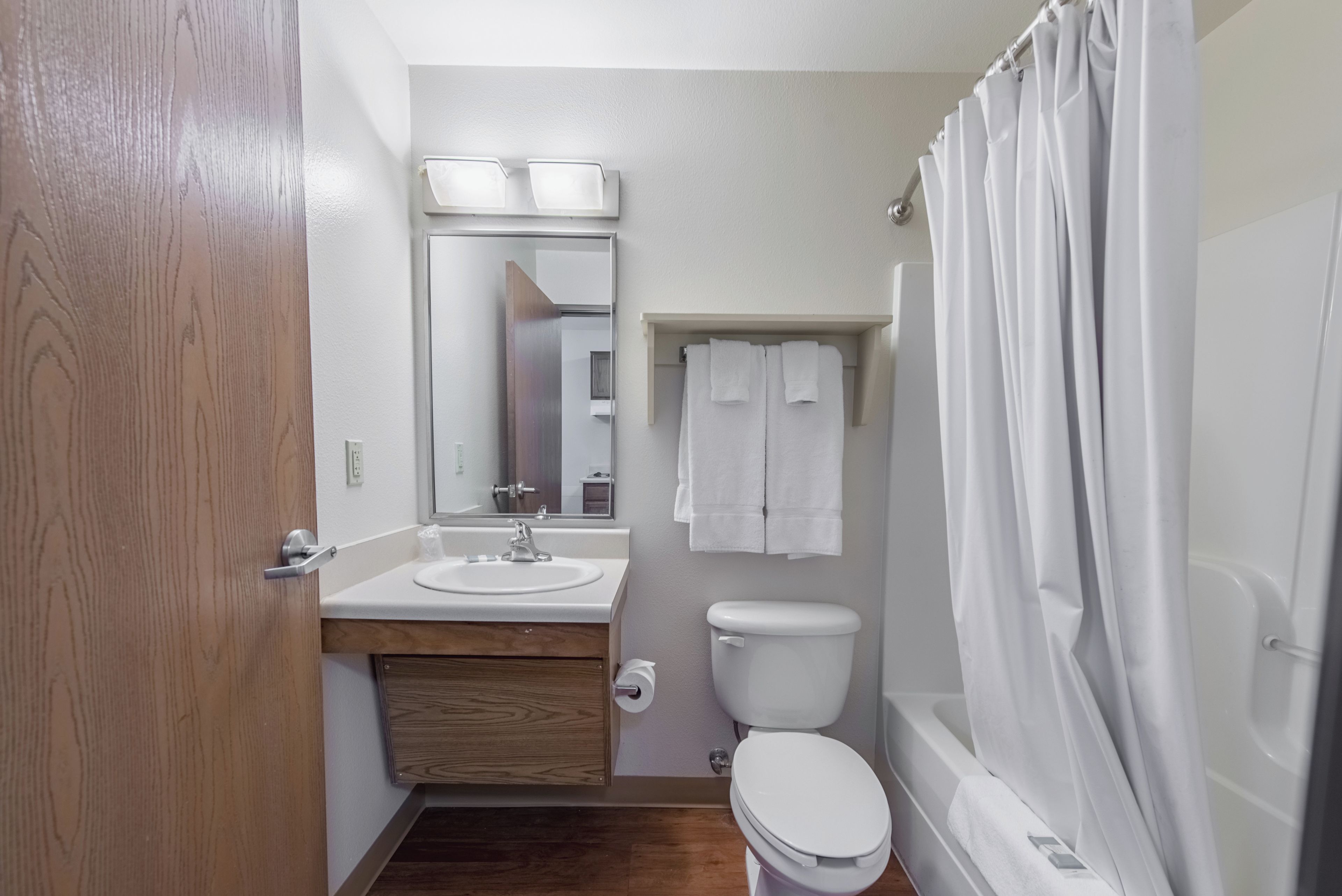 A bathroom with a wooden door, a sink, a toilet, a mirror, and a shower curtain.