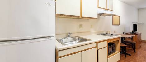 A kitchen with a white refrigerator, stainless steel sink, wooden cabinets, and a microwave.