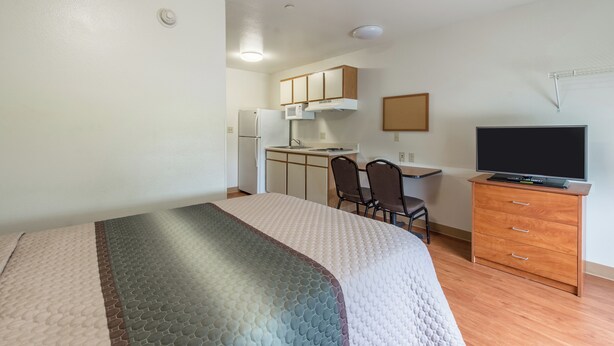 Een hotelkamer met een bed, een bureau, een stoel, een televisie en een kitchenette.